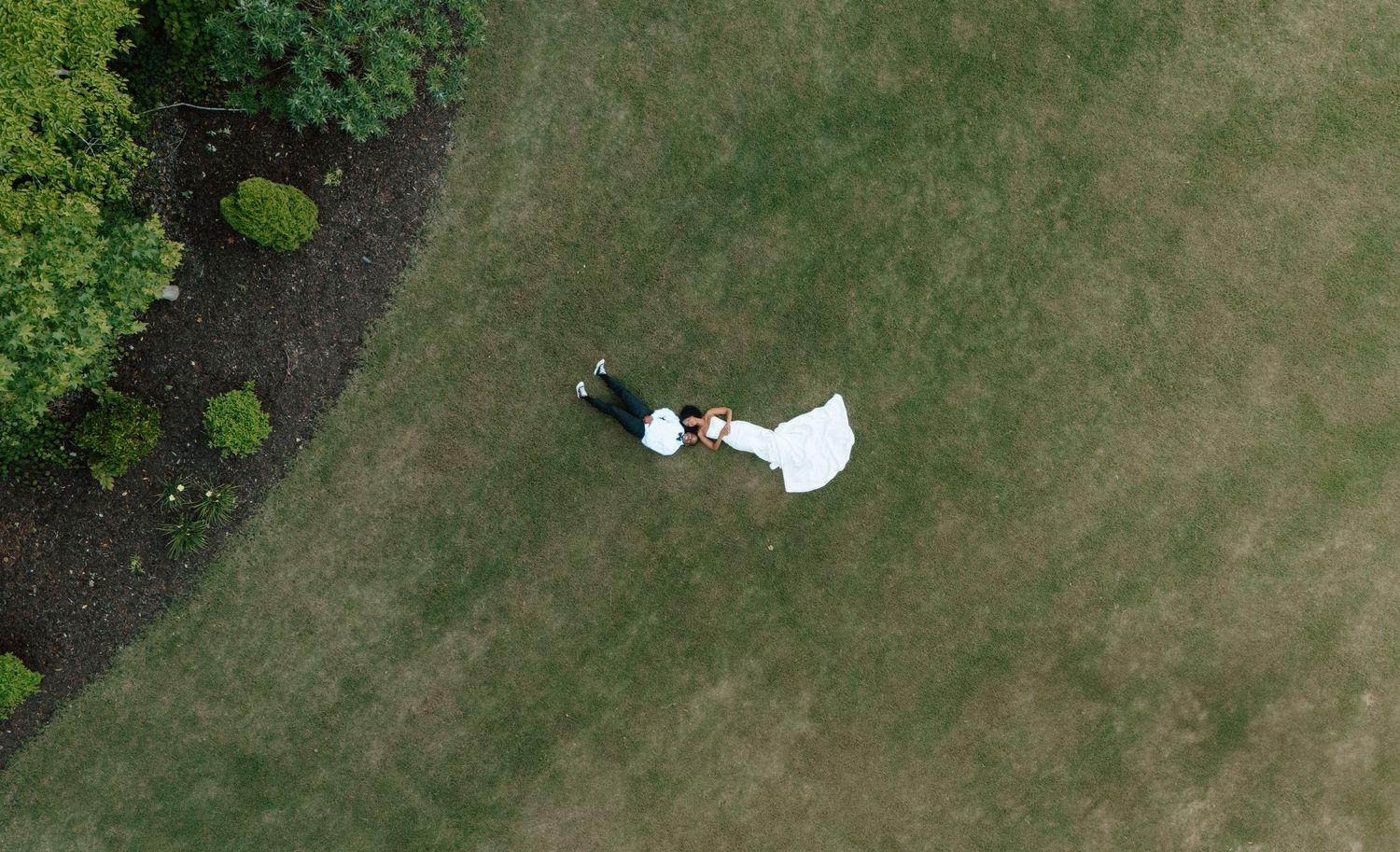 Aerial drone view of a bride and groom holding hands on a lush green lawn.