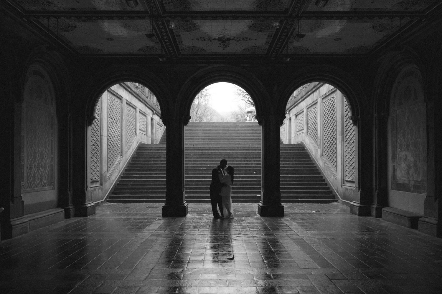 Couple sharing a romantic kiss under the arched colonnade of Bethesda Terrace in Central Park, black and white.