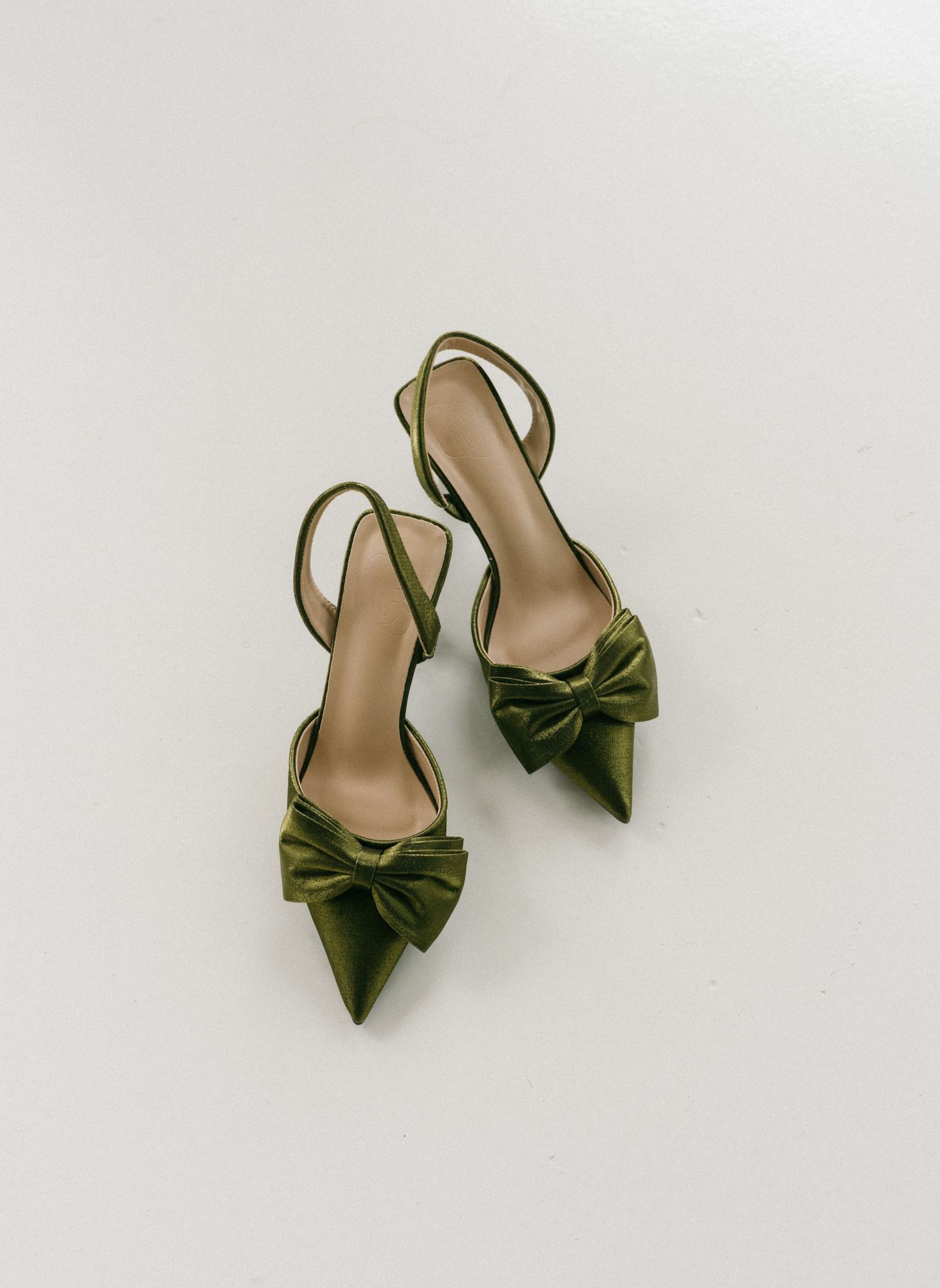 Olive green satin slingback heels with pointed toe and bow detail, displayed on white background.