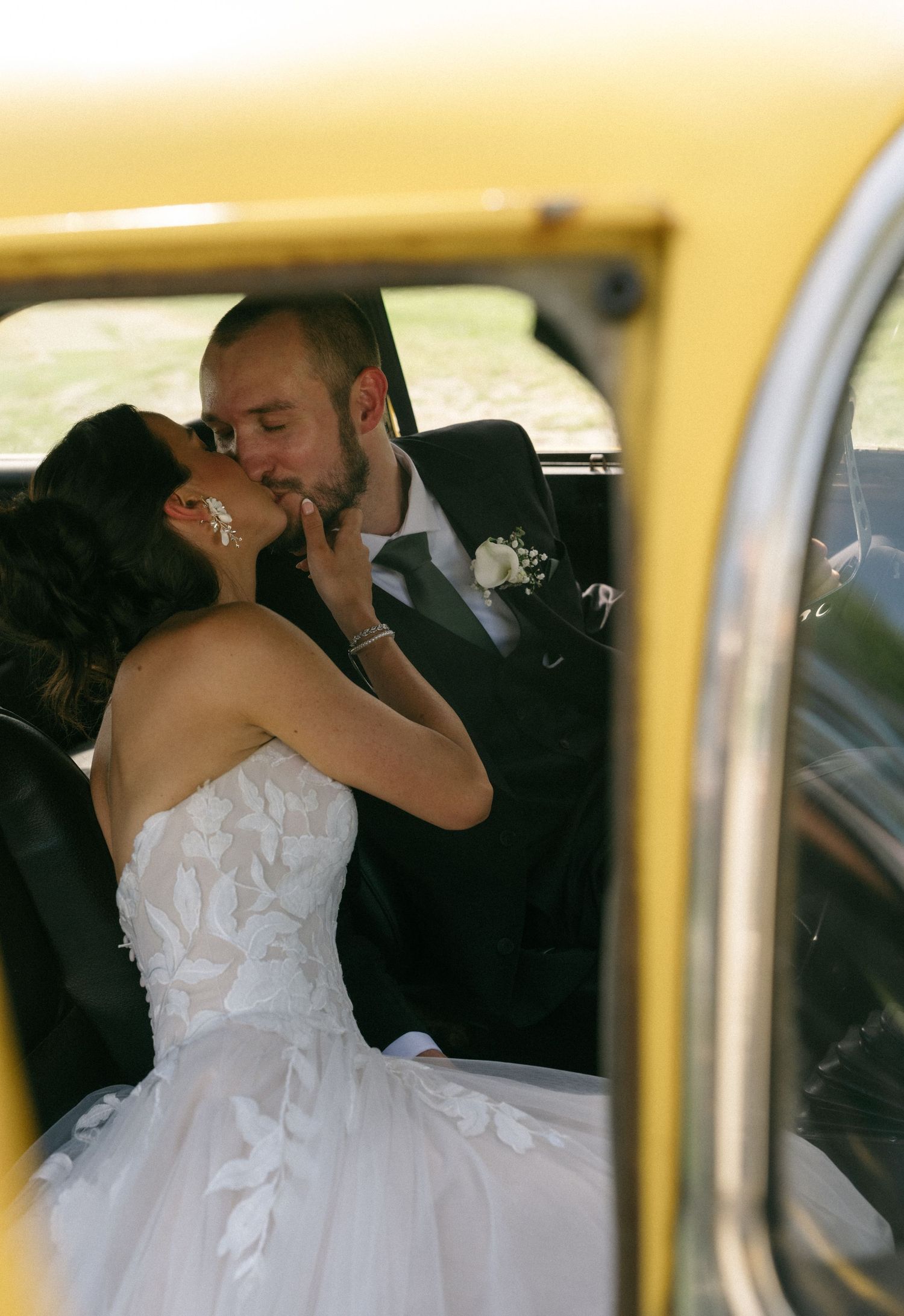 Bride and groom sharing a romantic kiss inside a vintage yellow car on their wedding day.