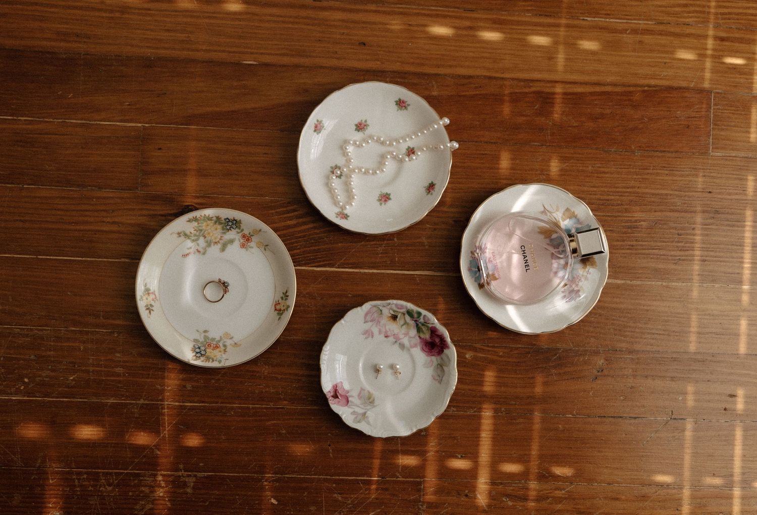 Four vintage floral porcelain saucer plates arranged on a wooden table, holding delicate jewelry pieces.