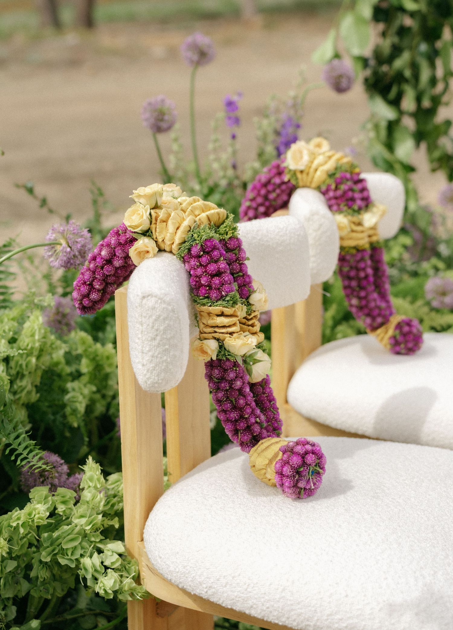 White chairs adorned with purple floral garlands and yellow roses at an outdoor wedding ceremony.