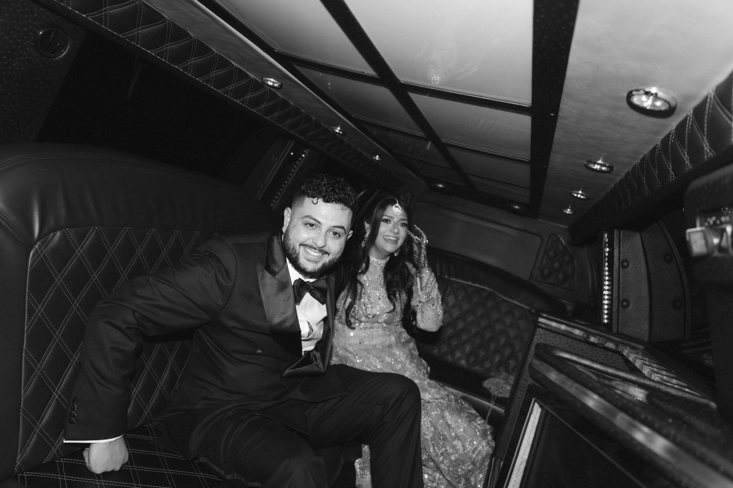 Couple smiling inside a limousine, dressed in formal attire, black and white photo.