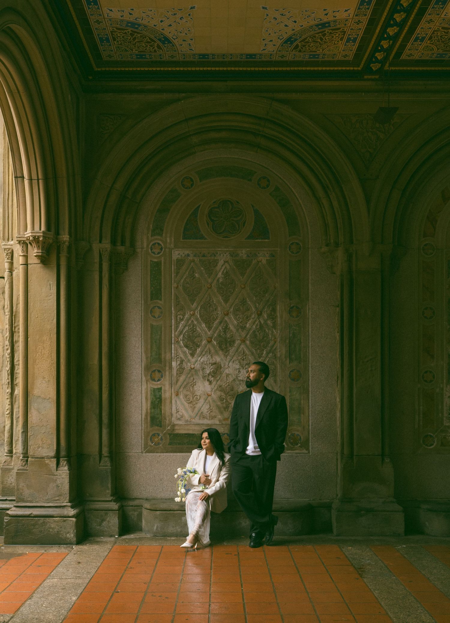 Couple in wedding attire posing under ornate arched ceilings at Bethesda Terrace in Central Park, NYC.