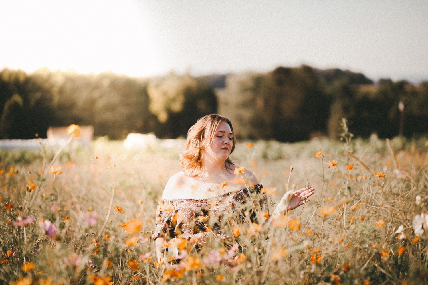 Woman in floral dress standing in a sunlit wildflower field, enjoying nature with golden hour light.