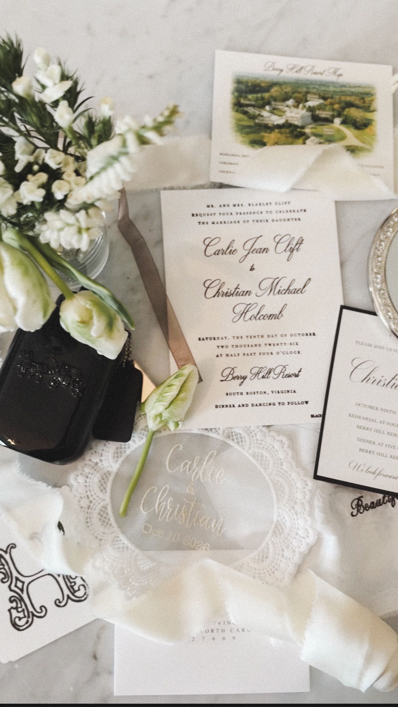 Elegant wedding invitation suite with floral script, white roses, acrylic place cards, and lace details on marble.