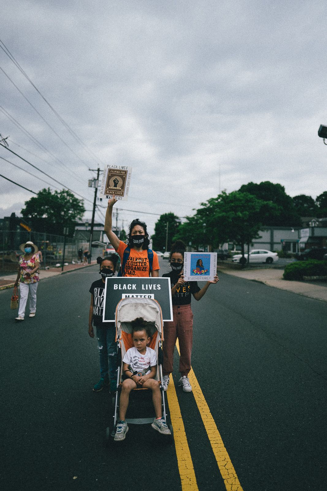 People marching in a Black Lives Matter protest on a cloudy day with power lines overhead.