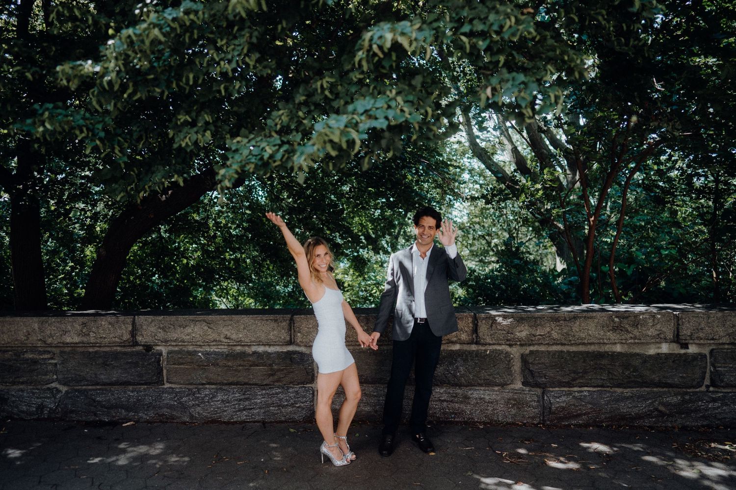 A couple enjoying a playful moment together on a stone wall surrounded by greenery.