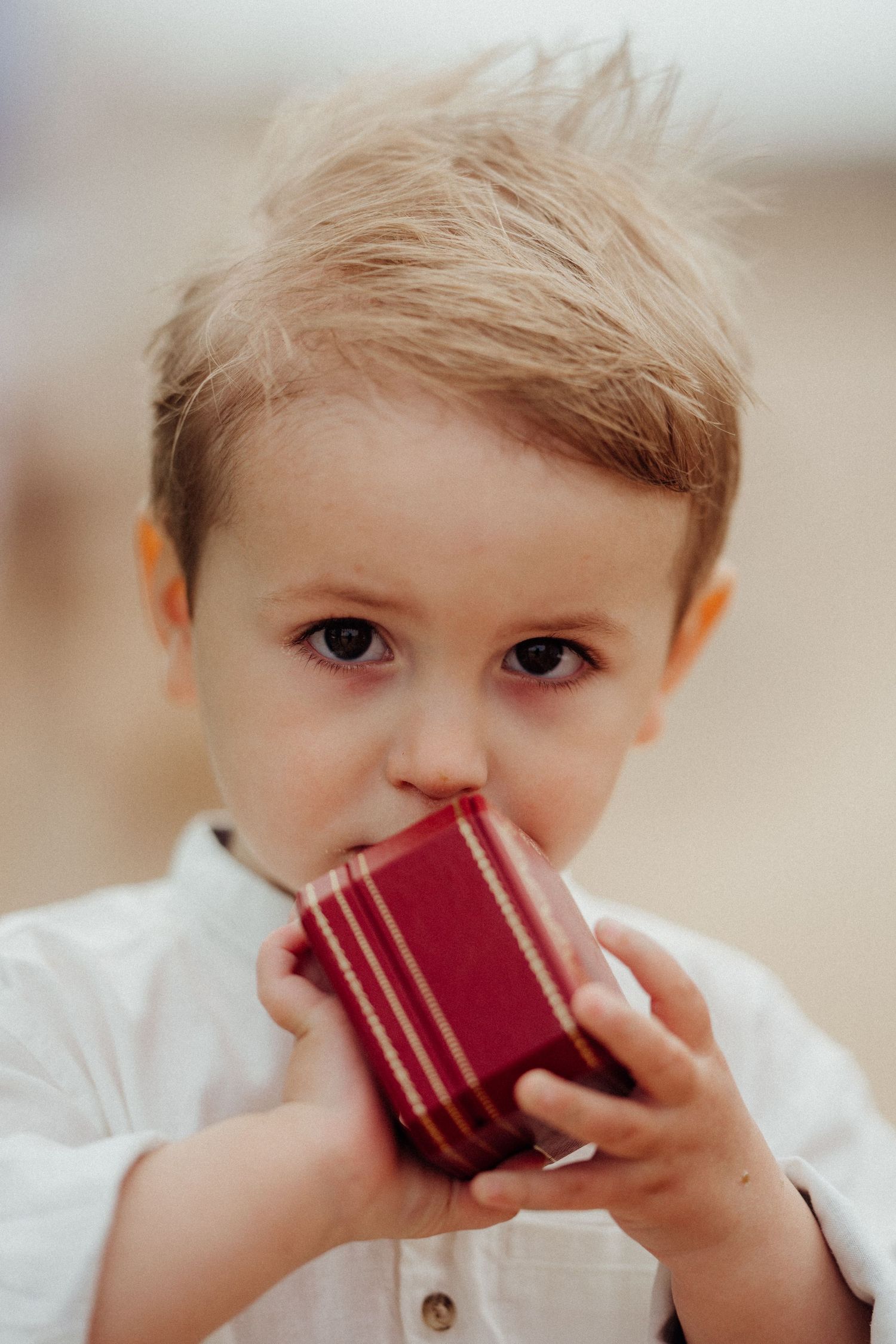 Young child in white shirt holds small red book close to face.