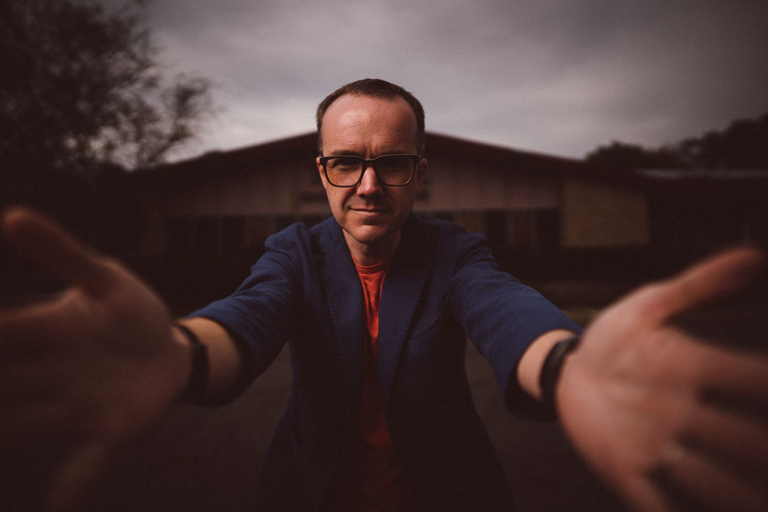 Wide angle selfie style photo showing person in glasses and blue jacket outdoors at dusk.