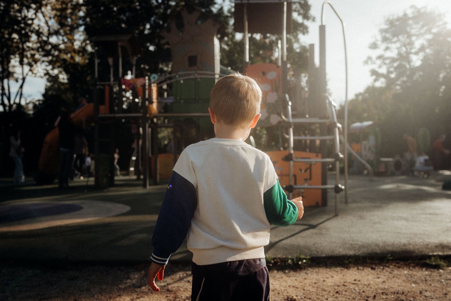 A child in a white shirt stands in a park during golden hour sunset.