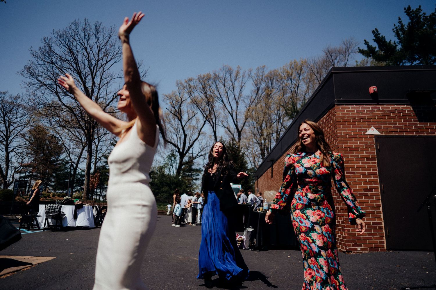 Group of women dancing with arms raised outside a brick building.
