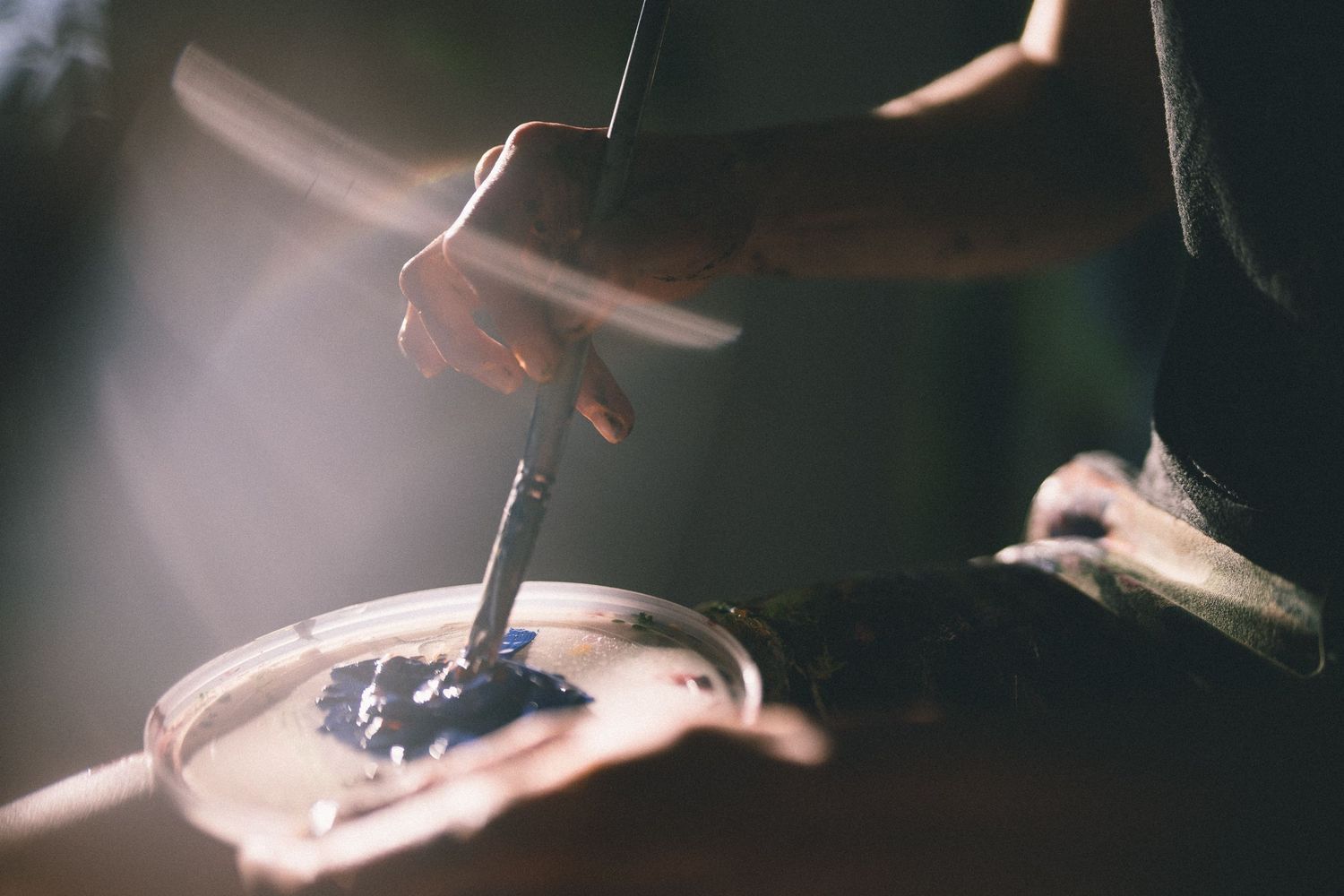 Close-up shot of hands mixing paint on an artist's palette in soft lighting.