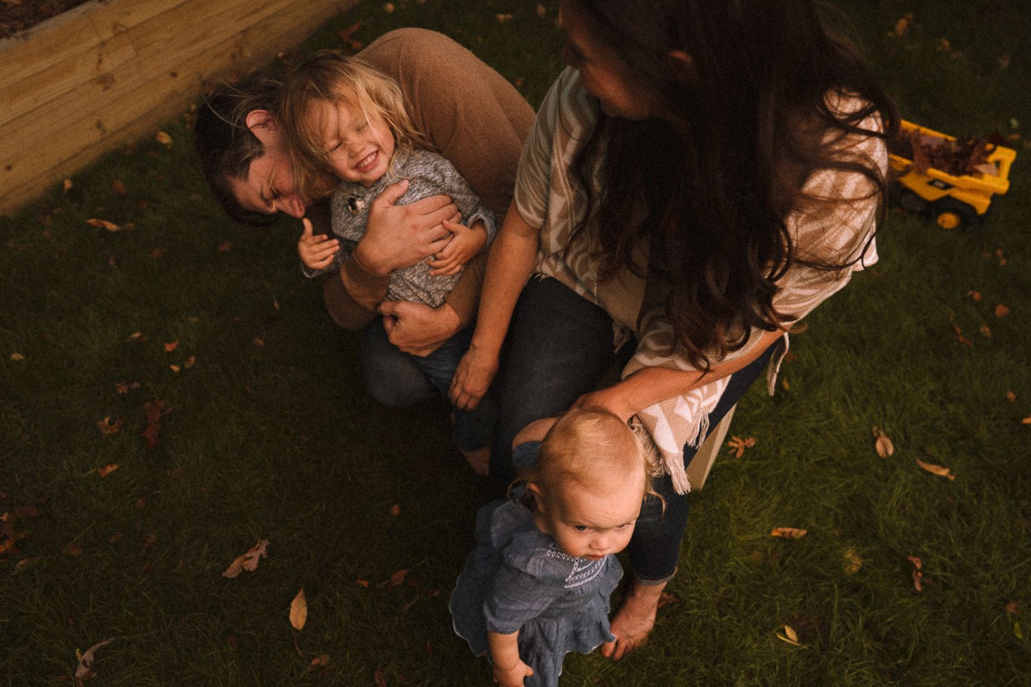 A family playing and laughing together on grass during an outdoor photo session.