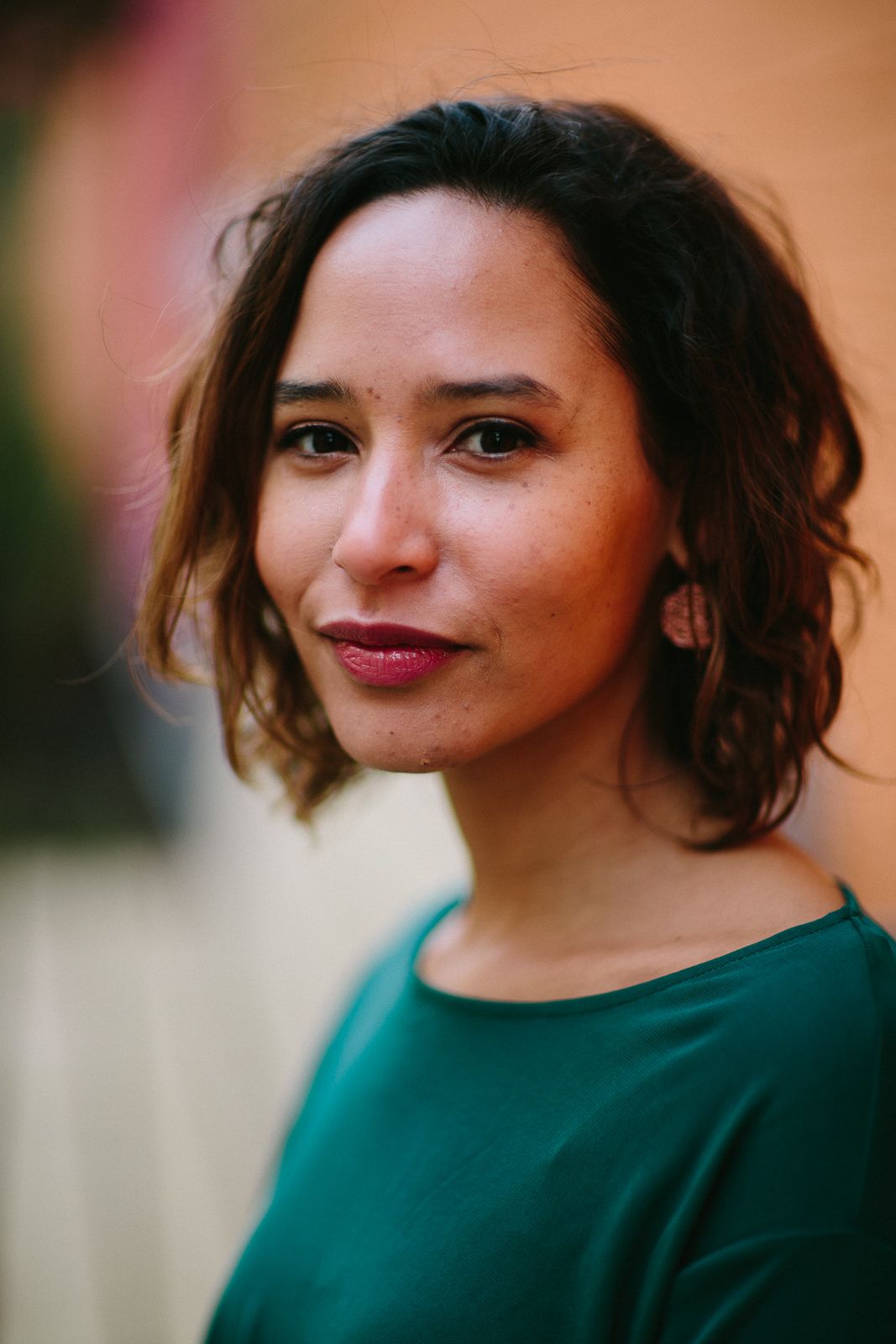 A woman in a green top poses against a warm-colored background with natural lighting.