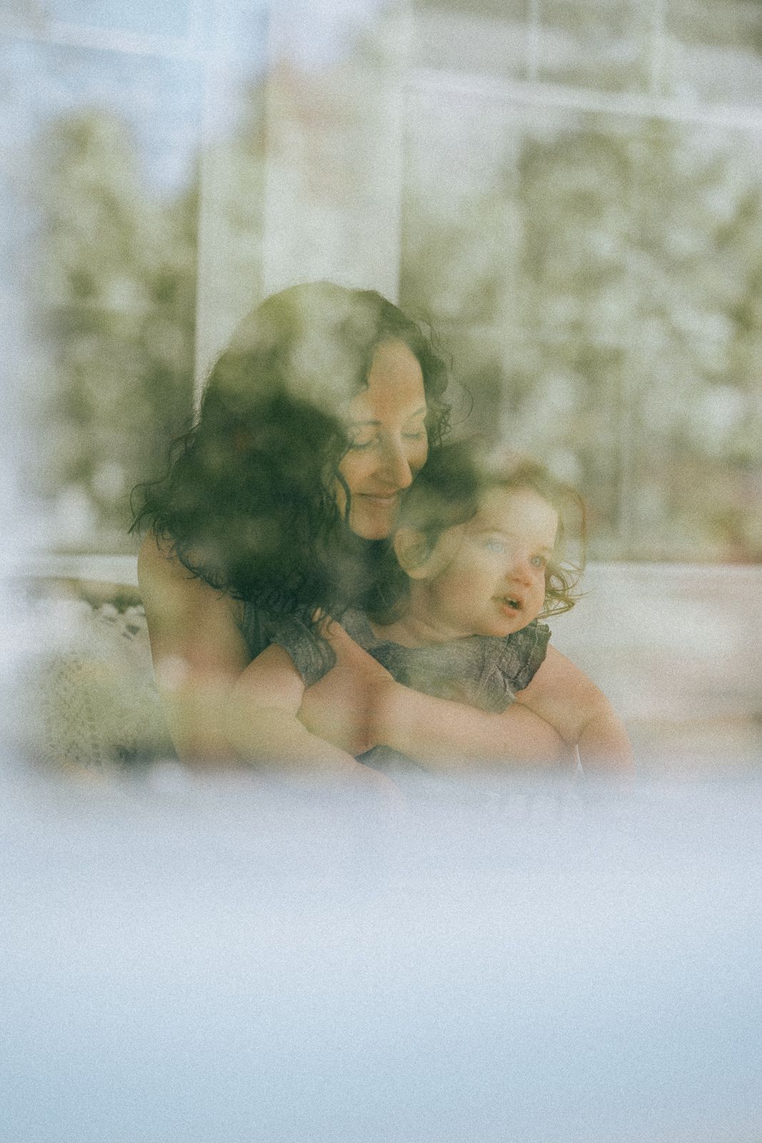 A dreamy, soft-focus portrait of a parent and child through sheer curtains.