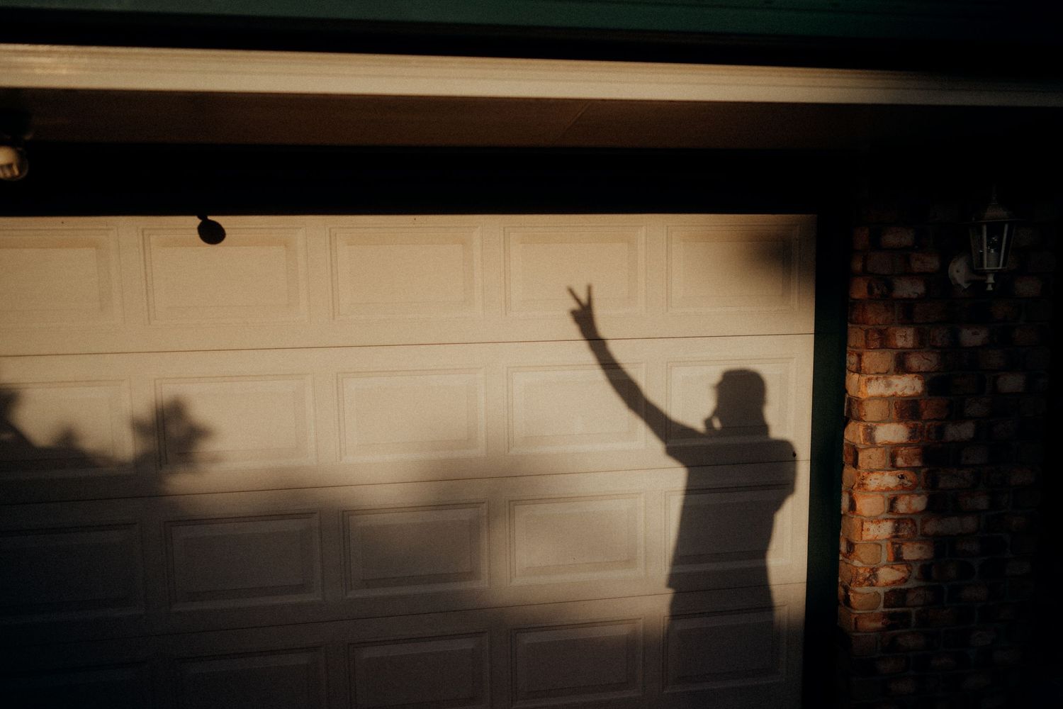 Shadow of person making peace sign gesture on garage door at sunset.