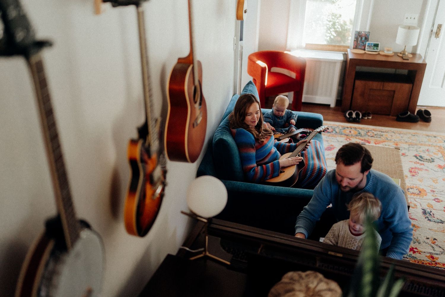 Musical instruments hang on wall while people relax in cozy living room setting.