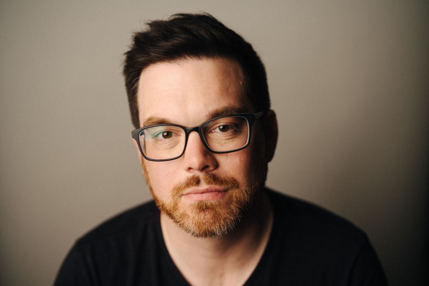 Portrait of person wearing glasses and black shirt against neutral background.