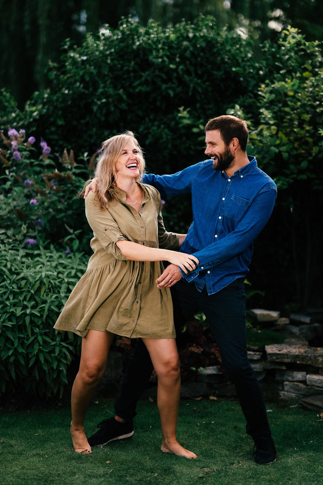 A joyful couple laughing and dancing together in a garden setting.