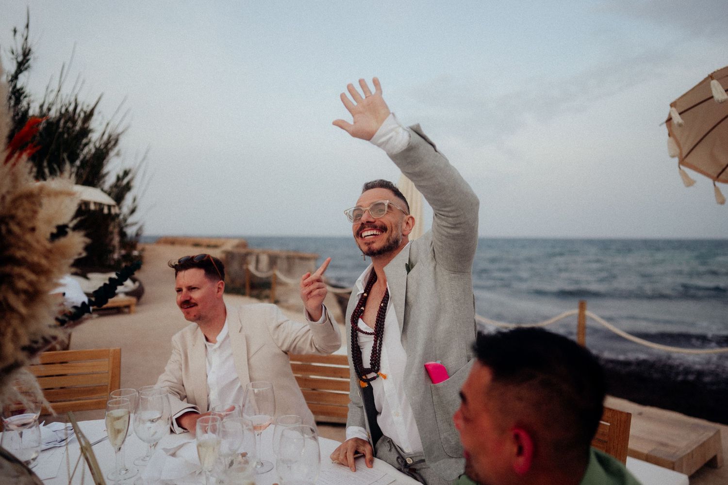 Wedding reception guests celebrate at outdoor seaside dinner table.