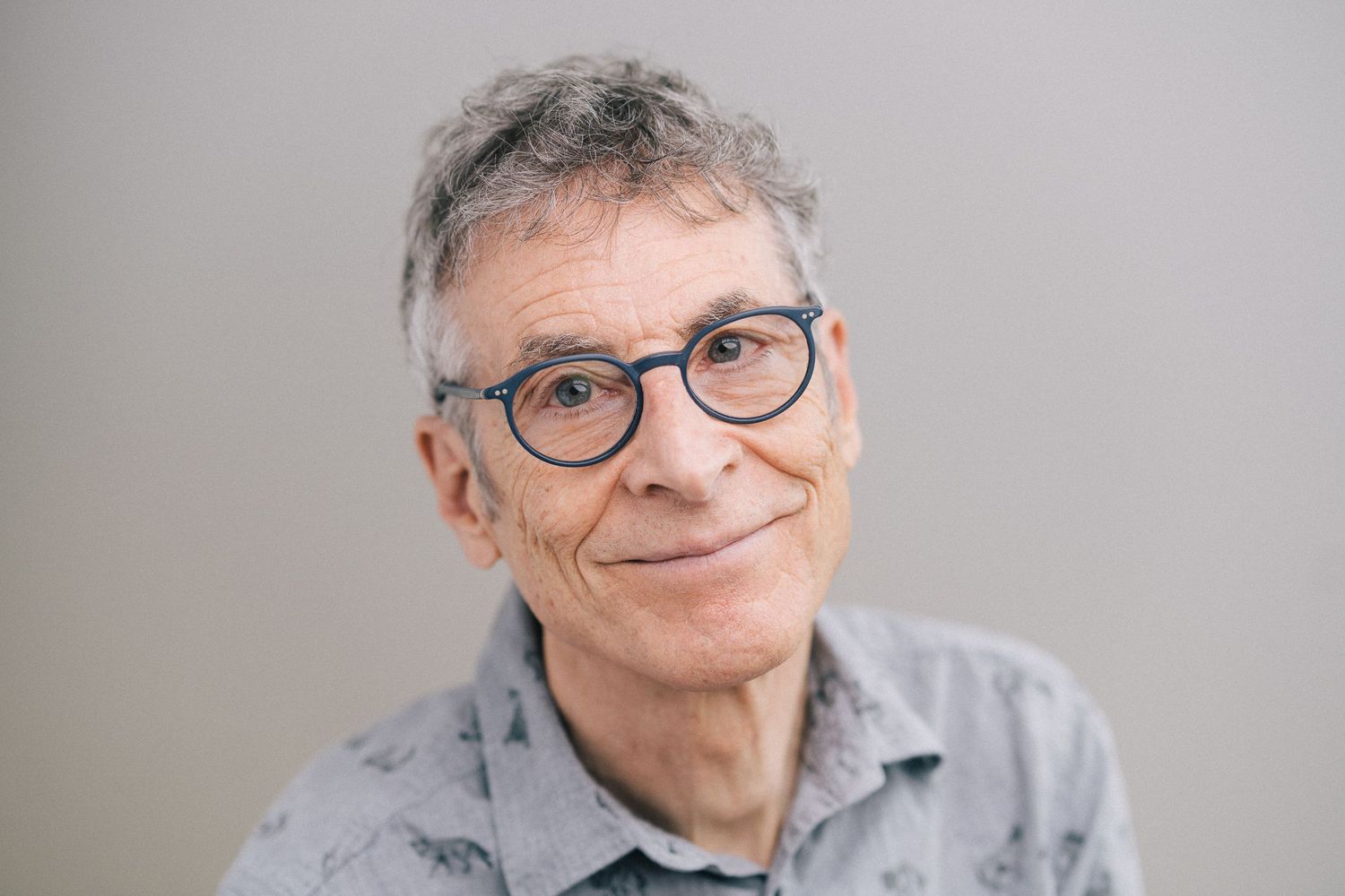 Portrait of a person wearing glasses and a gray shirt against a neutral background.