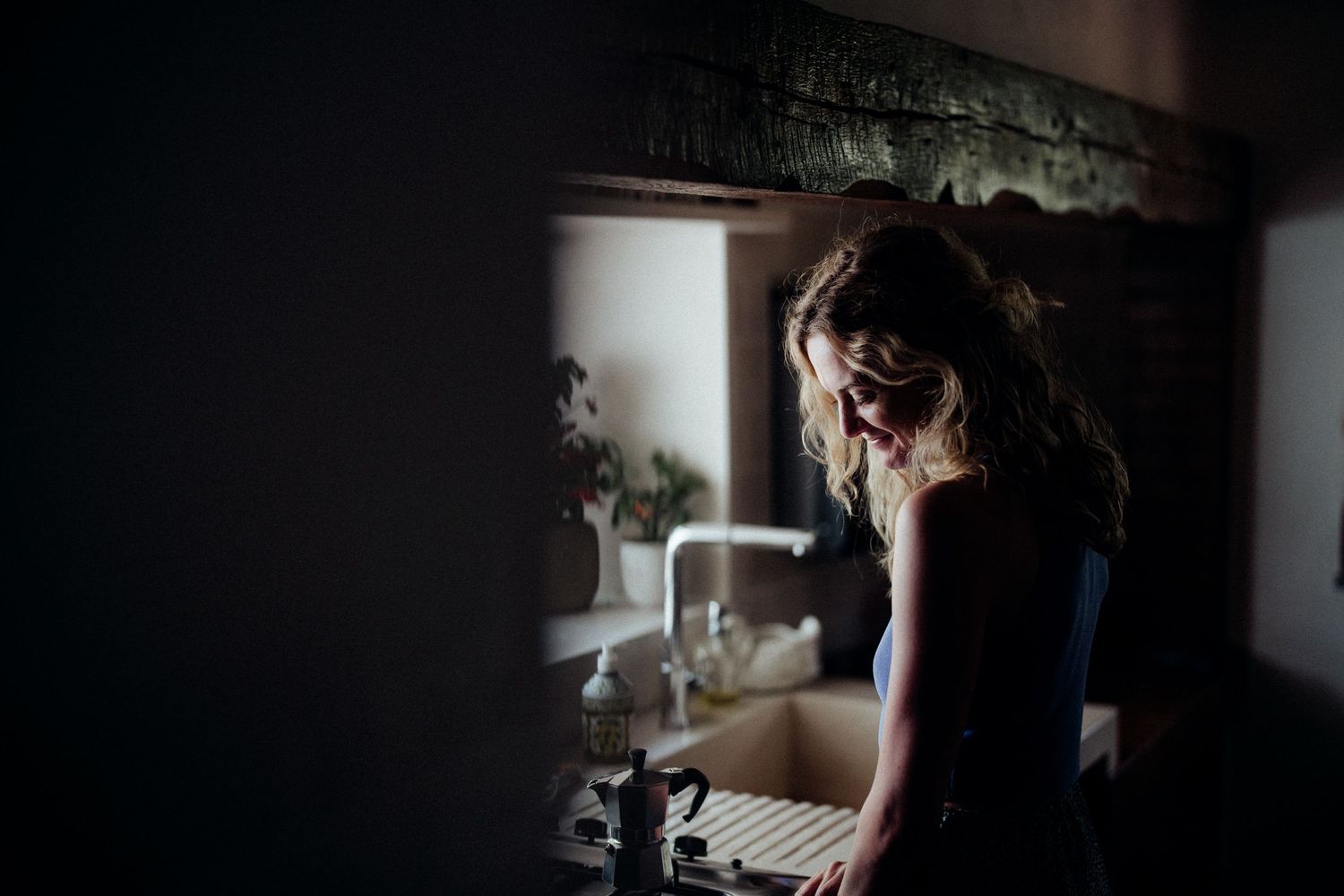 Dark atmospheric photo of person at kitchen sink with window light.