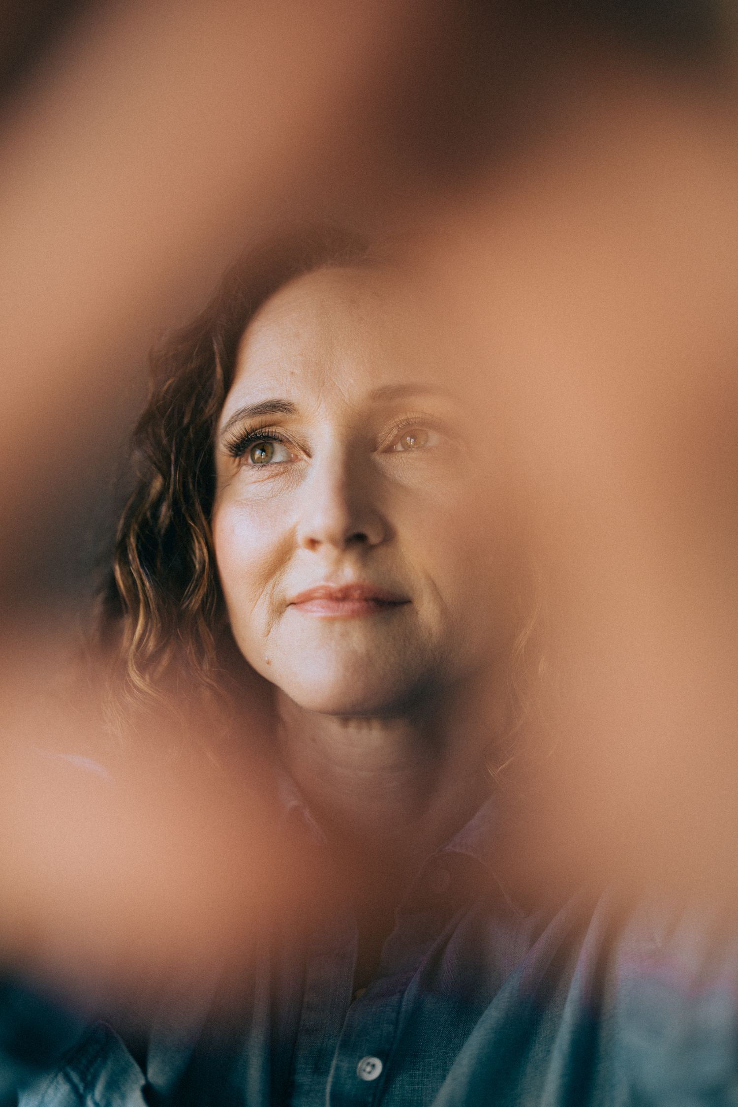 Artistic portrait with soft focus and warm tones showing contemplative expression through foreground blur.