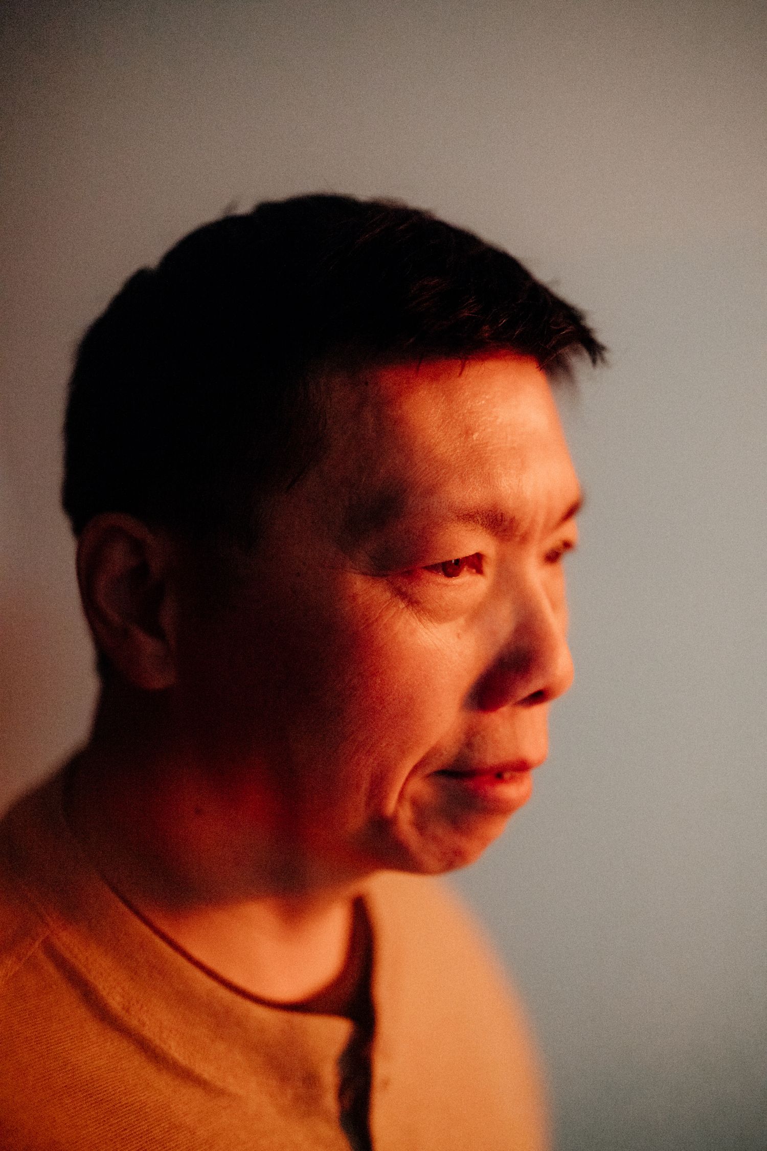 Portrait in warm lighting showing person in orange shirt against neutral background.