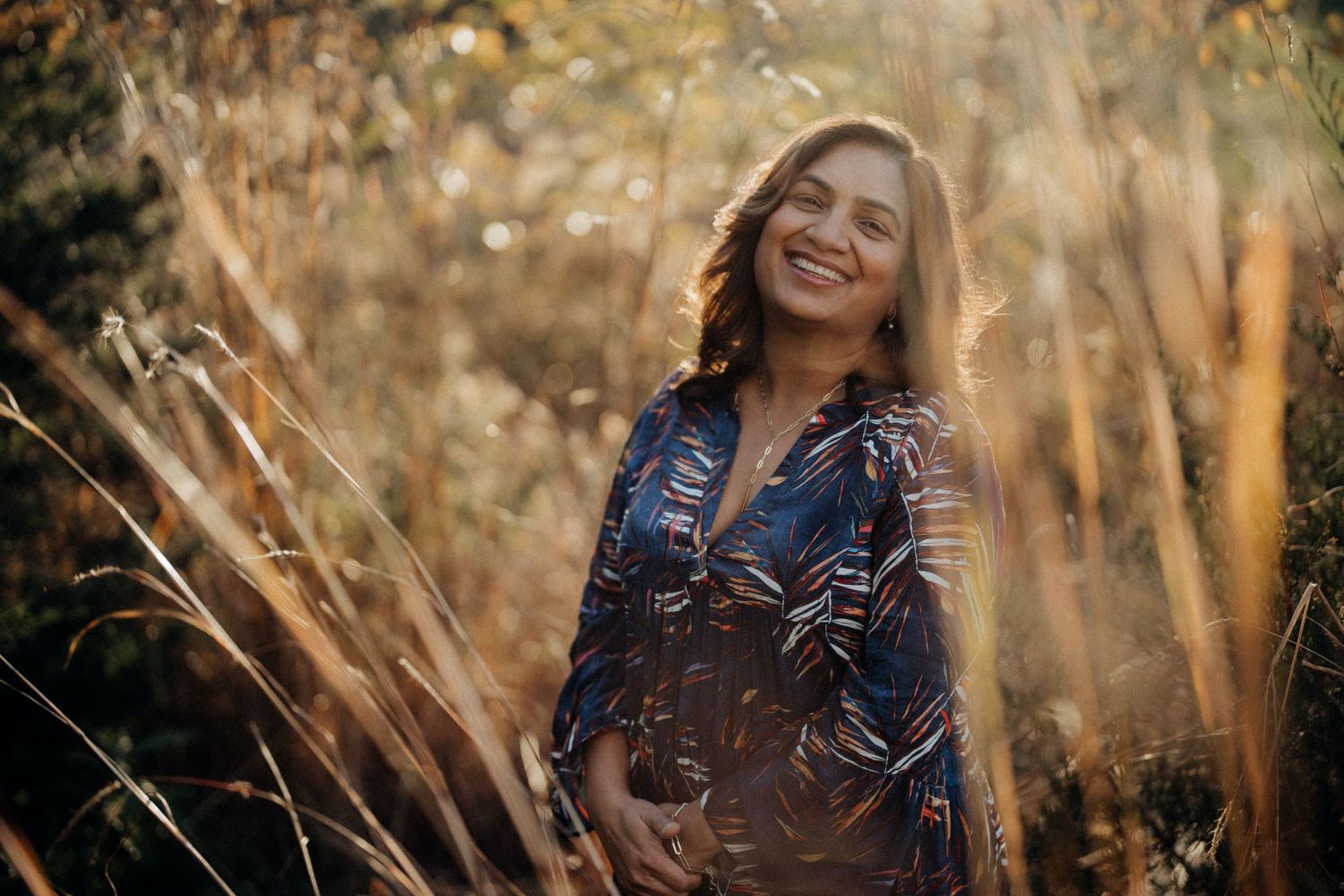 A glowing maternity portrait captured in golden light among tall grass.