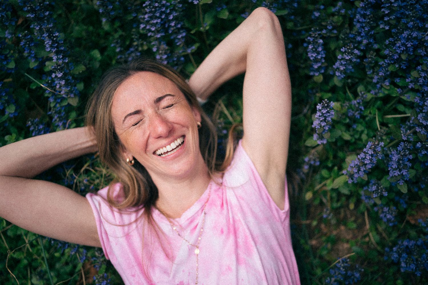 Person lying in field of purple flowers wearing tie-dye shirt.