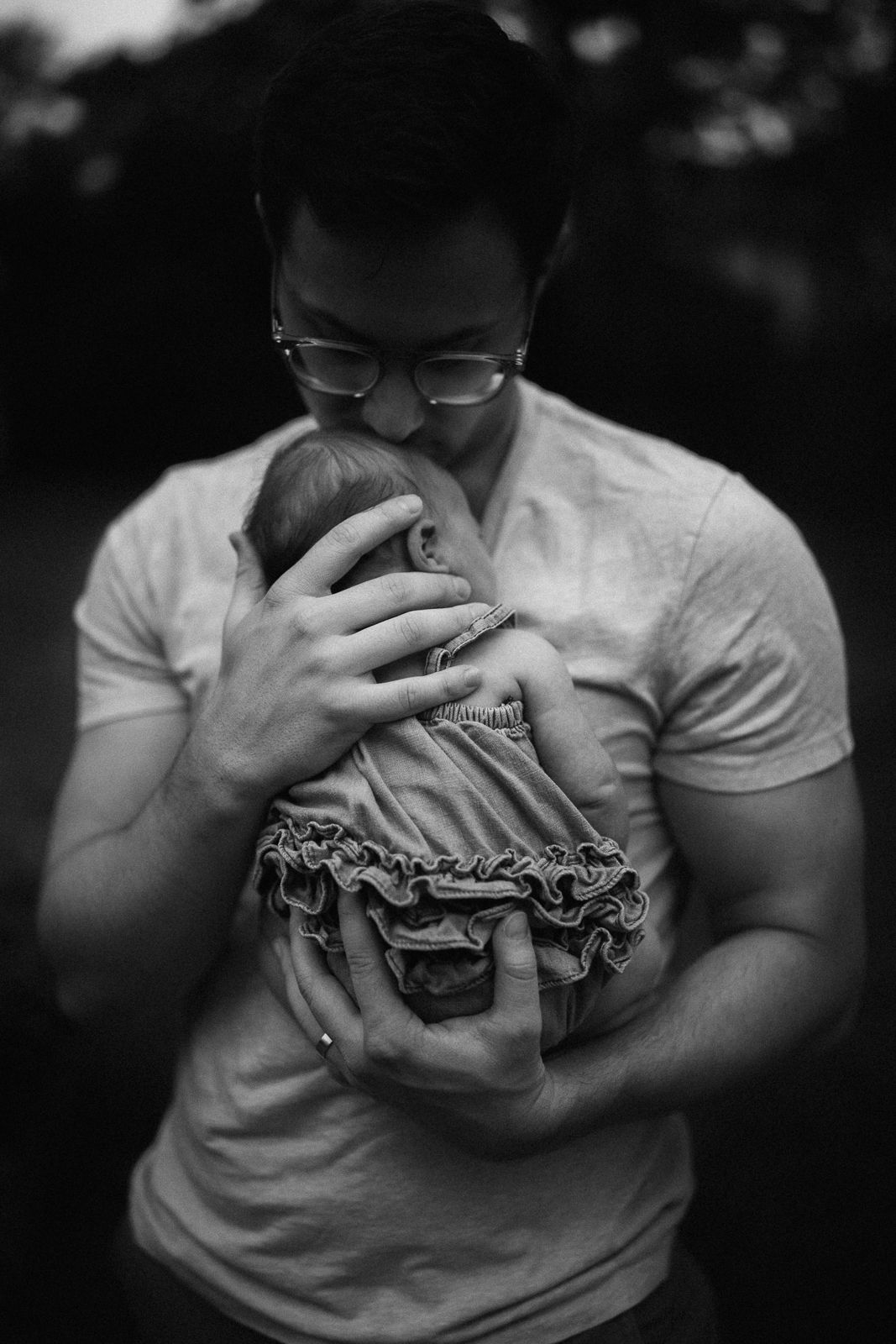 Black and white portrait of a parent tenderly holding a baby in a ruffled dress.