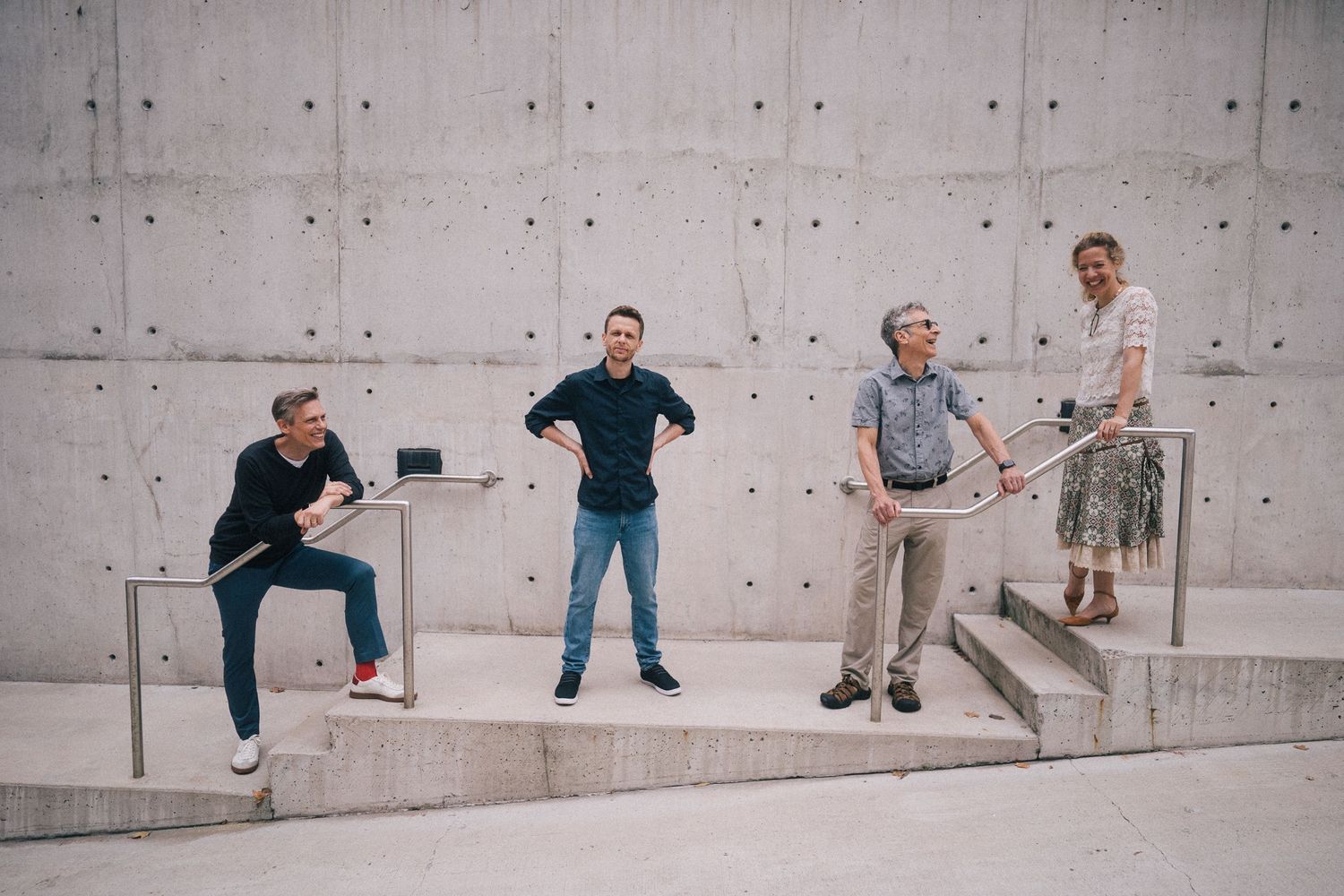 Four people posing playfully on concrete steps against a minimalist gray wall.