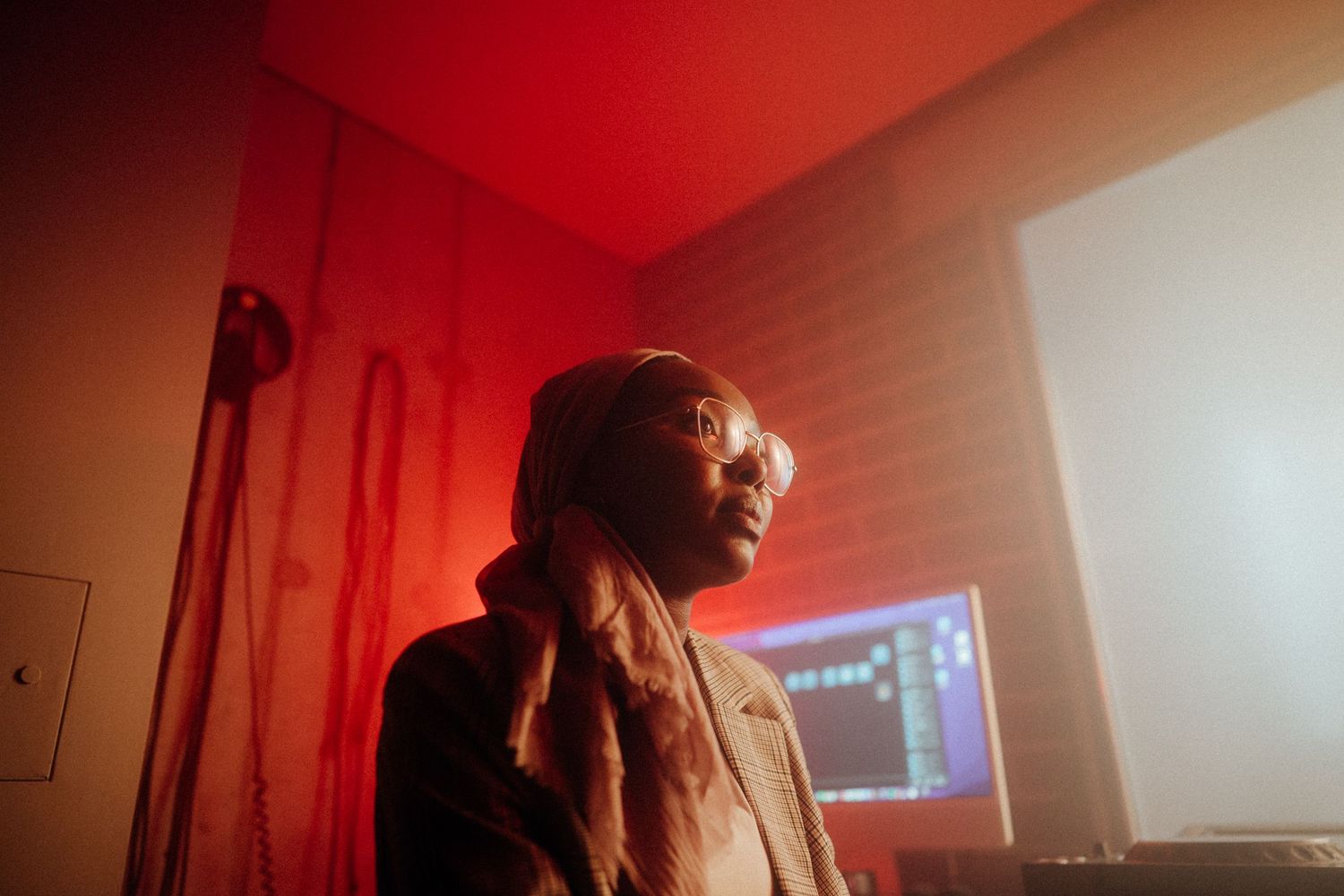 A moody red-lit studio scene with dramatic lighting and a computer screen visible in the background.