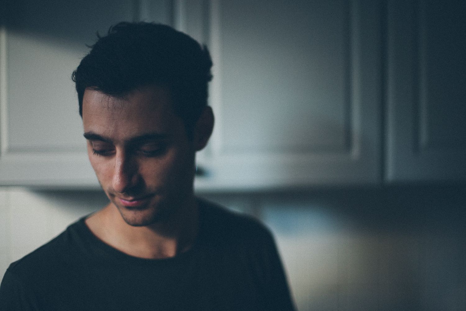 Moody portrait of someone in dark clothing looking down against blurred background.