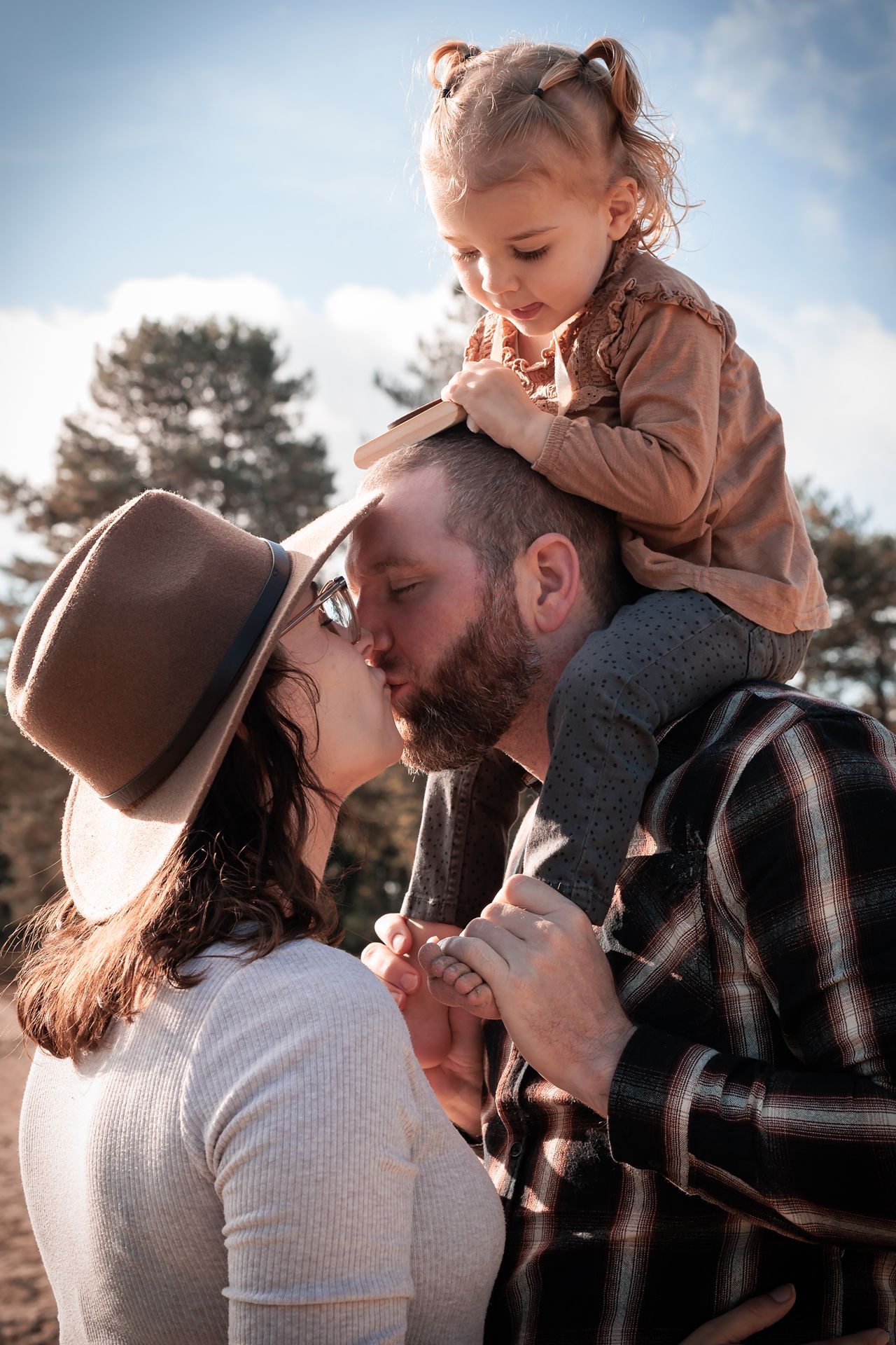 Koppel dat elkaar kust en peuter die in de nek van haar papa zit tijdens gezinsfotoshoot in Bergen op Zoom