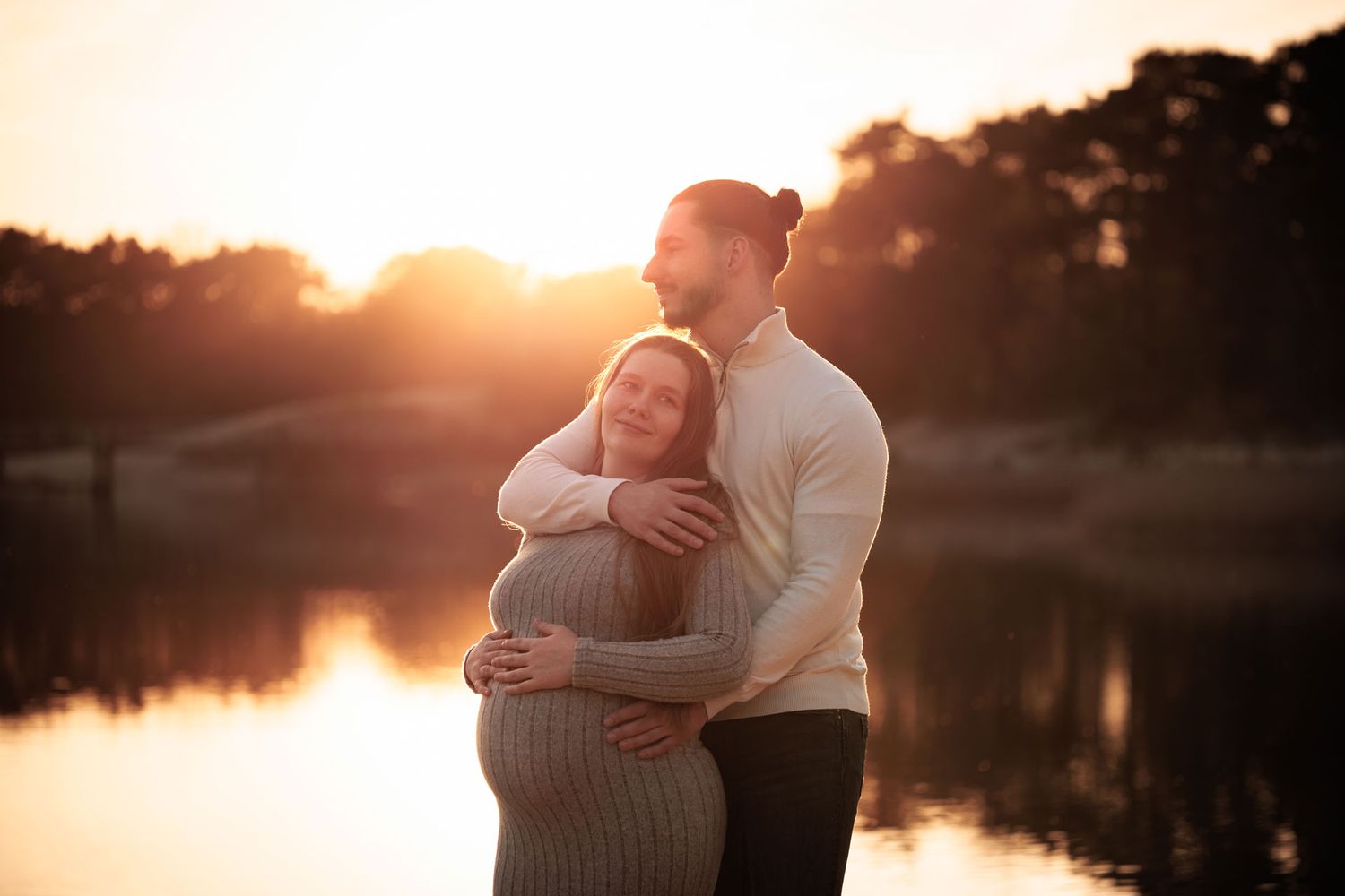Zwanger koppel knuffelend aan de waterkant met ondergaande zon tijdens zwangerschapsfotoshoot in Bergen op Zoom