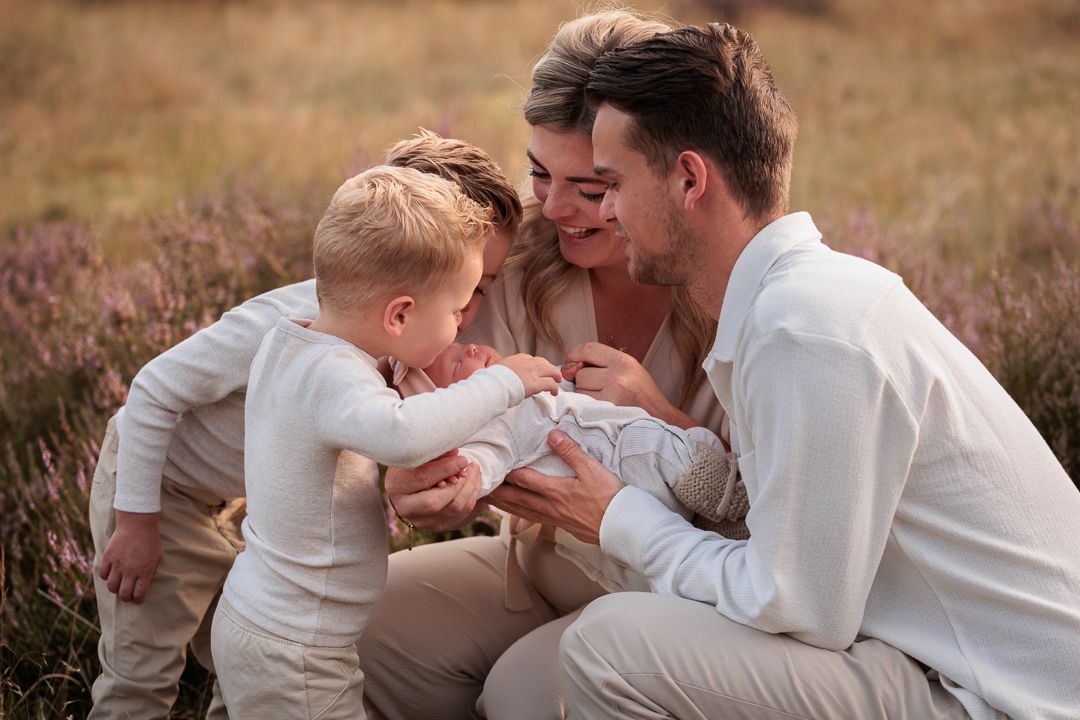 vrolijke foto van vader en moeder die gehurkt hun newborn baby dragen en twee broertjes haar van dichtbij bekijken