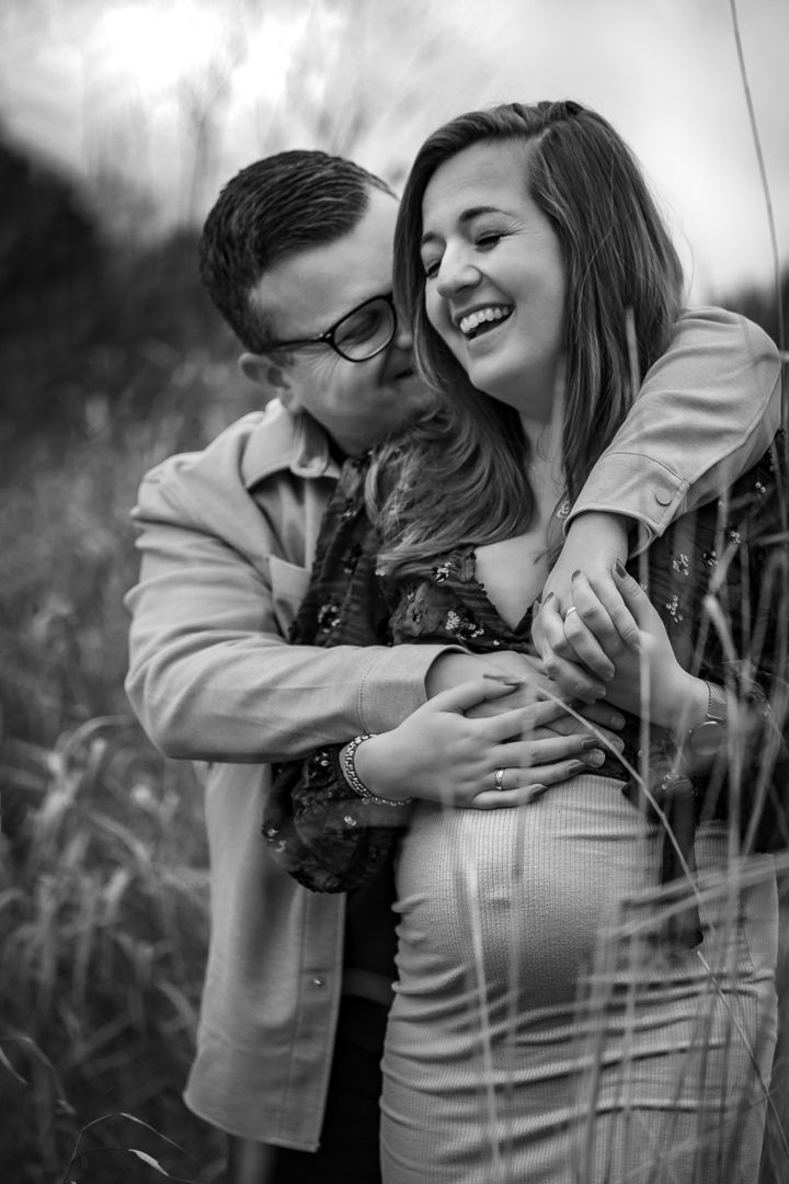 zwangere vrouw met haar partner lachend, half verscholen tussen het riet