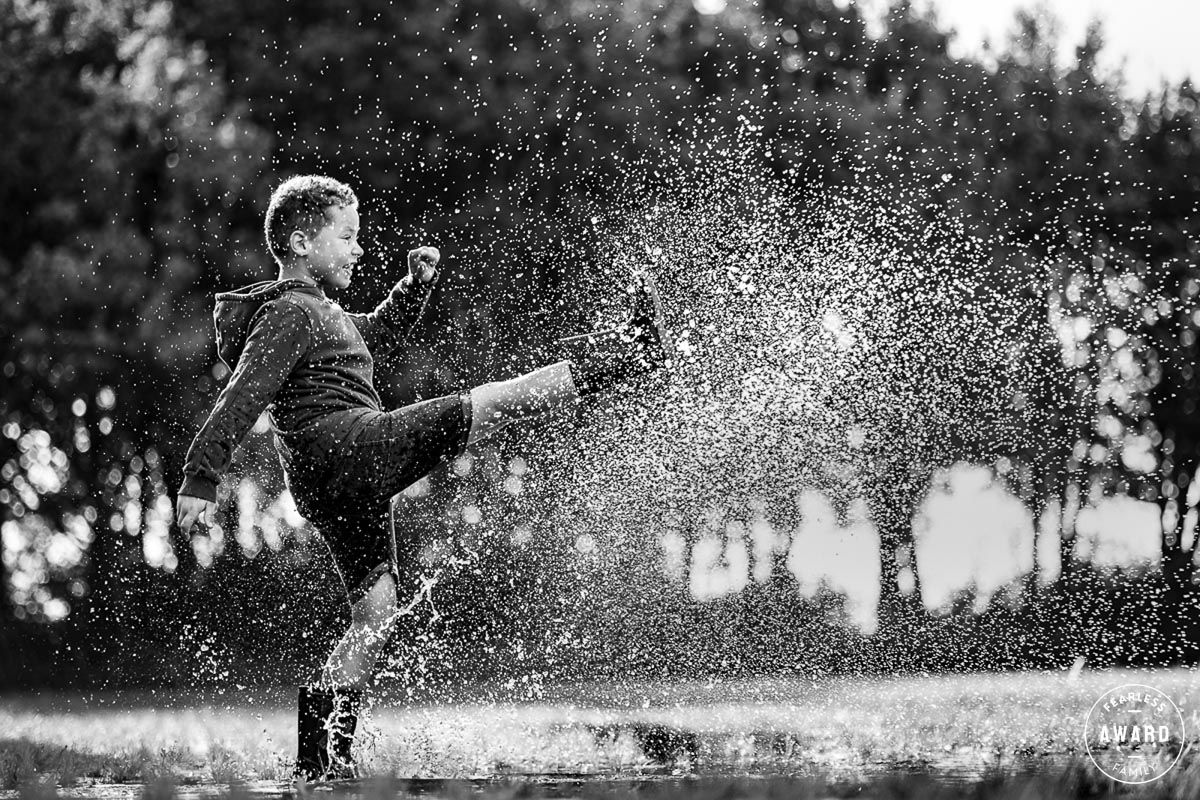 Jongen schoppend in een regenplas waardoor het water opspat, prijswinnende foto van Fotos van Jess in Fijnaart