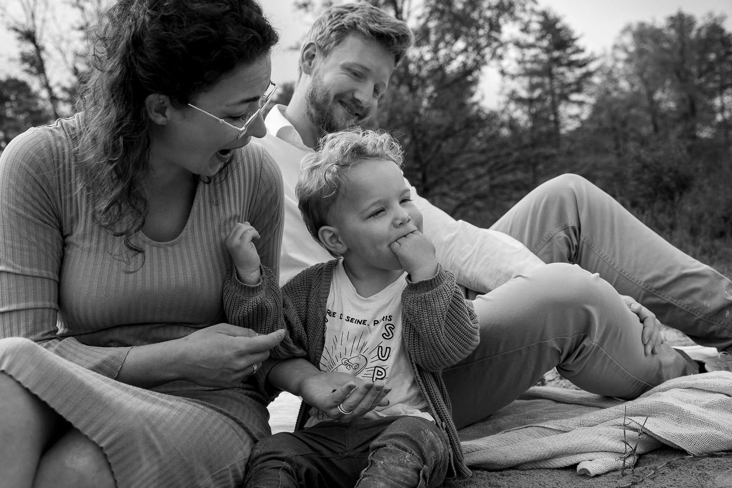Grappig moment tijdens gezinsfotoshoot waar gezin op een kleedje zit en met elkaar speelt en lacht - fotograaf