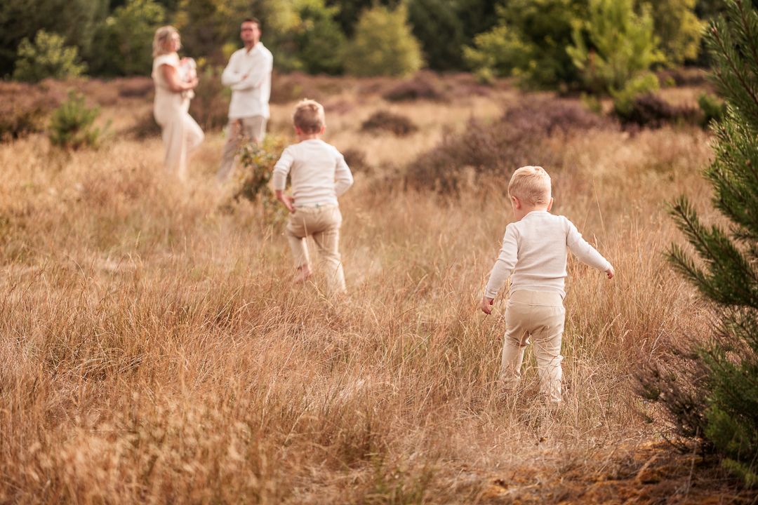 jonge kinderen rennen over het veld naar hun ouders tijdens ongedwongen buiten fotosessie in de natuur