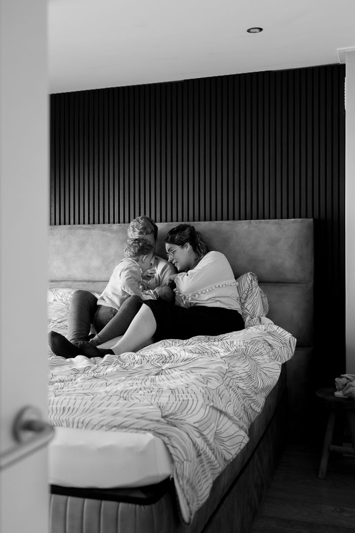 inkijkje in de ouderlijke slaapkamer waar het gezin met newborn baby op bed zit
