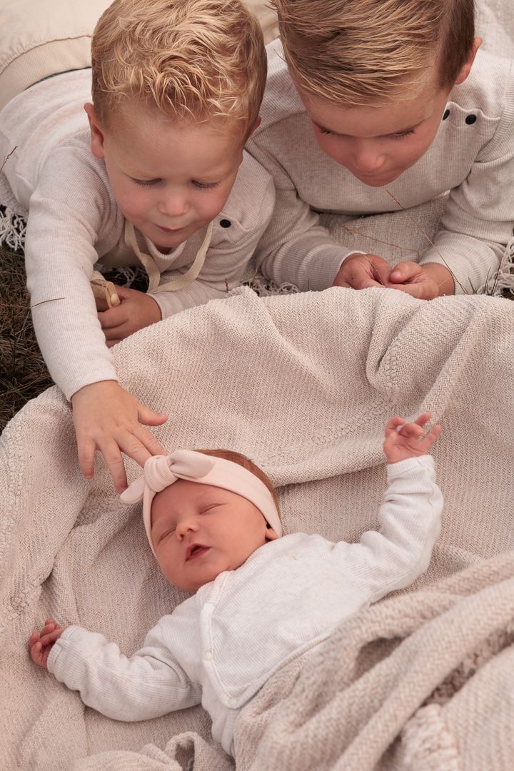 broertjes nieuwsgierig kijkend in het babymandje waar hun newborn zusje in ligt, zachtjes aaiend over haar hoofdje. echte momenten