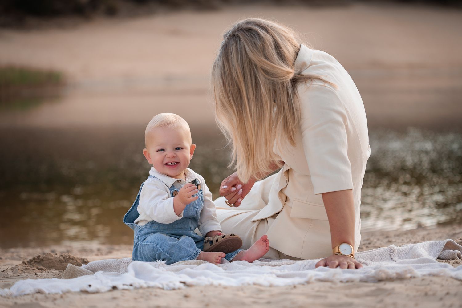Moeder knuffelt haar jonge kind tijdens intieme motherhood fotoshoot aan de waterkant
