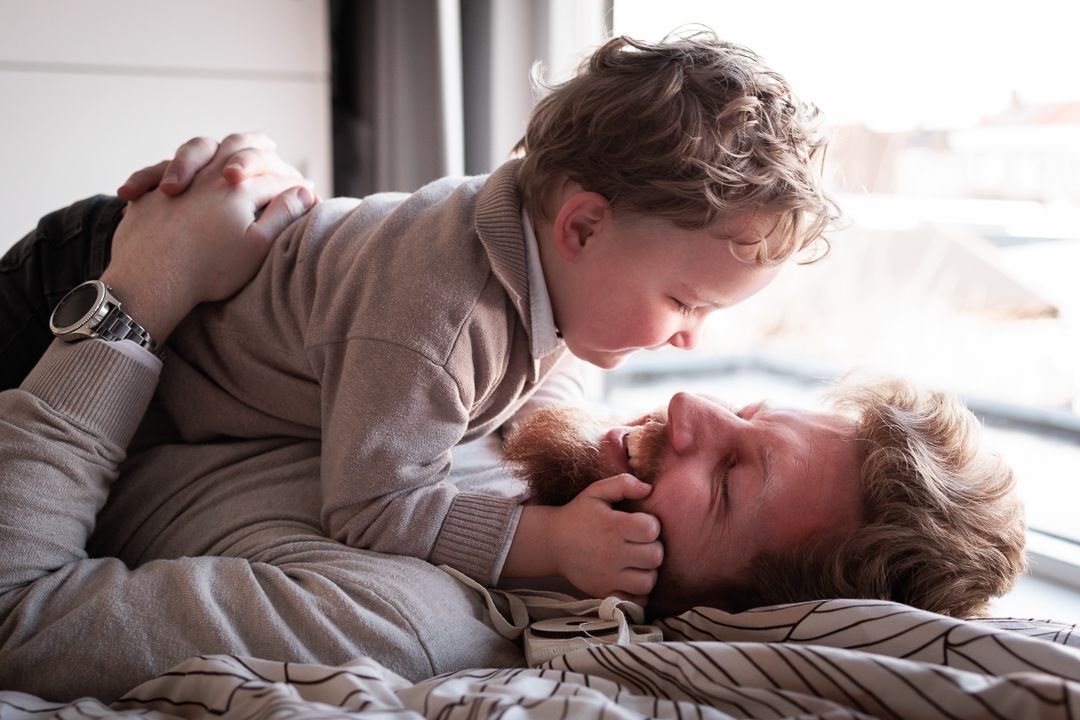 vader een zoontje op bed stoeiend en lachend tijdens newbornsessie