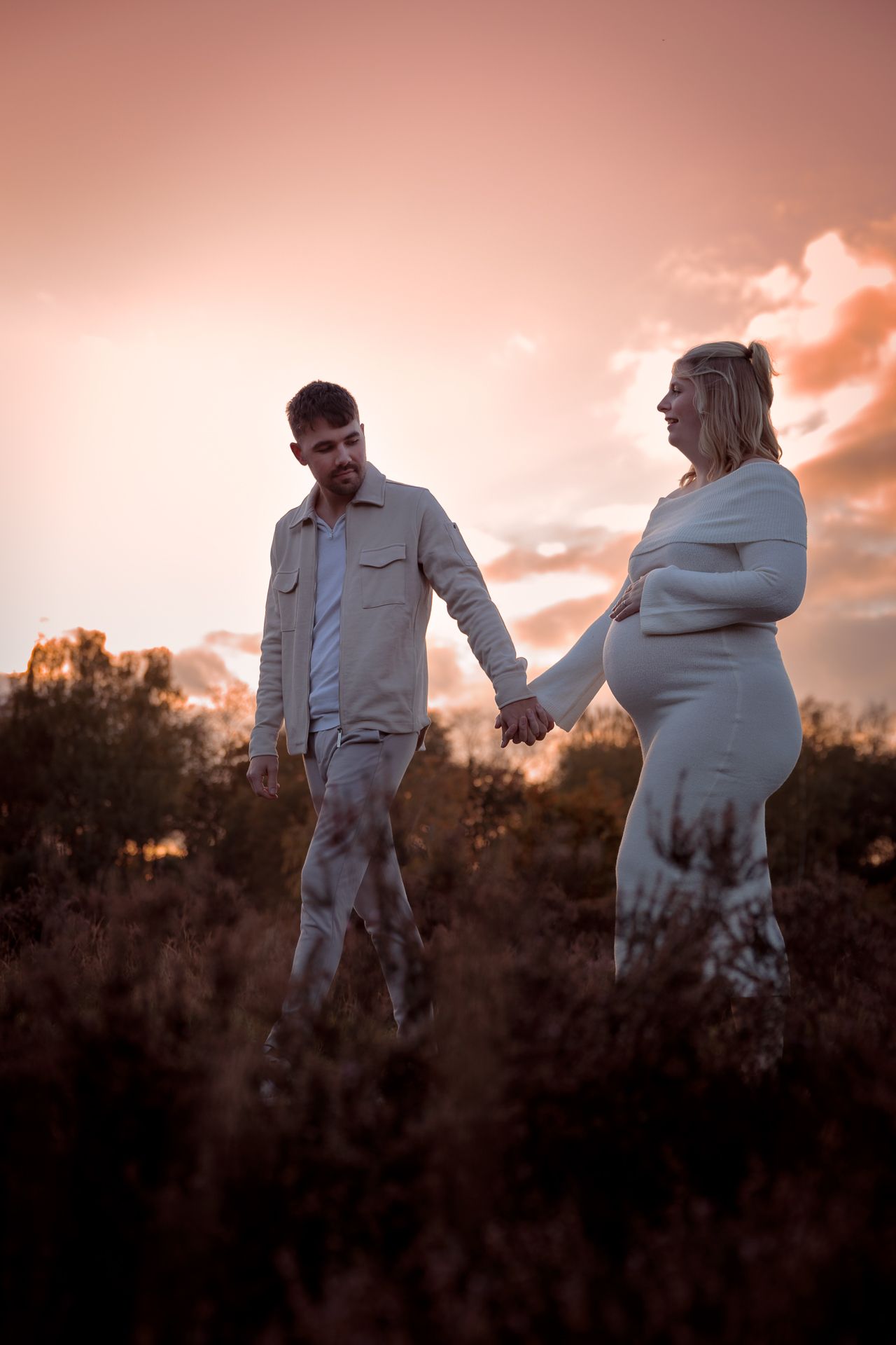 voorbij lopend zwanger koppel tussen het hoge gras op een mooie fotoshoot locatie in Bergen op Zoom tijdens zwangerschapsfotoshoot