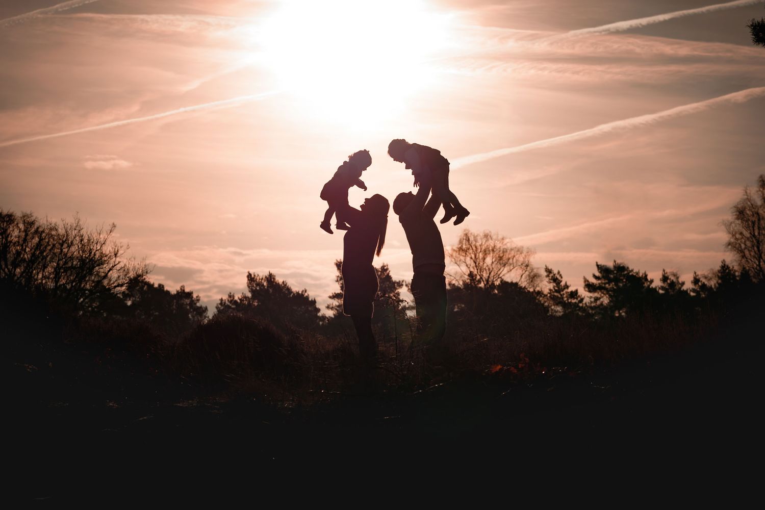 Lifestyle gezinsfotografie met silhouettefoto van ouders en kinderen samen buiten, liefdevolle familie momentopname door gezinsfotograaf.