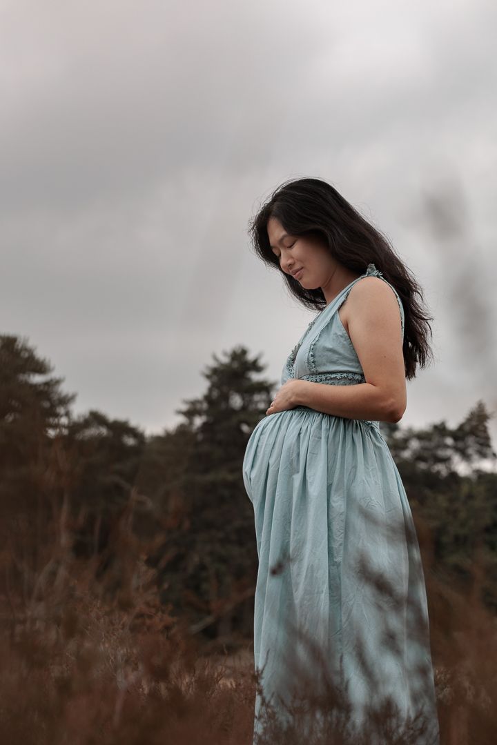 Zwangere vrouw in zwierige jurk tijdens zwangerschapsfotoshoot in moody landschap van Bergen op Zoom