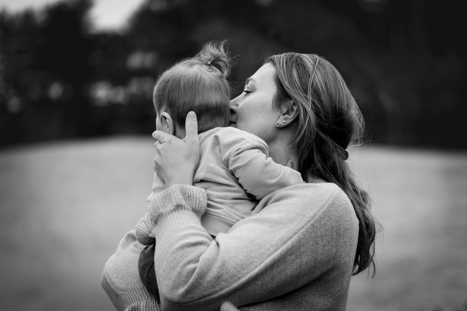 Intieme motherhoodfotoshoot – moeder knuffelt haar jonge kind tijdens ontspannen sessie buiten in West-Brabant.